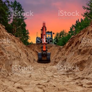 Excavator dig trench at forest area on amazing sunset background. Backgoe on earthwork for laying crude oil and natural gas pipeline or water main pipes. Construction the sewage and drainage
