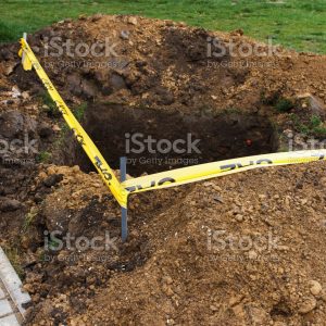 A square pit dug into the soil, next to public sidewalk and fenced with a yellow ribbon, as a sign of danger. Communal service works, eliminate problems underground